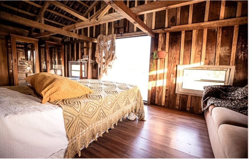 Quarto Iceland com cama queen, sofá e paredes de madeira rústica no Celeiro