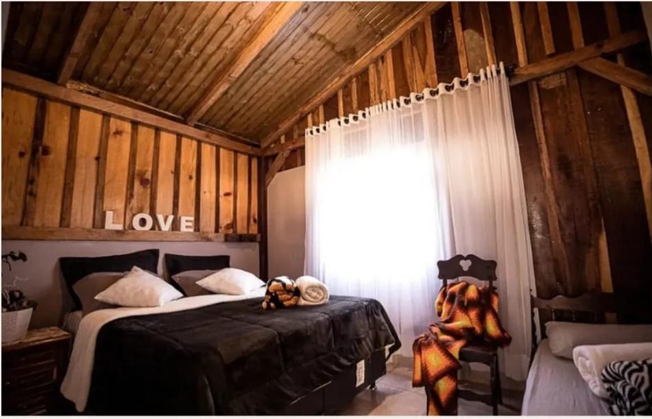 Quarto Alaska com cama queen e janela iluminada no Celeiro Guarapuava
