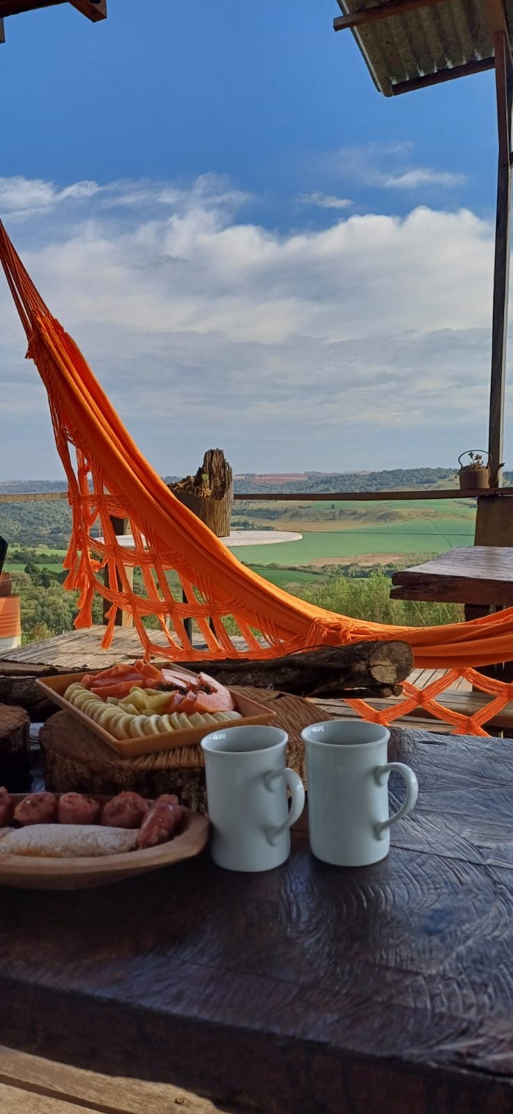 Café da manhã servido no deck, com rede laranja e vista para o campo